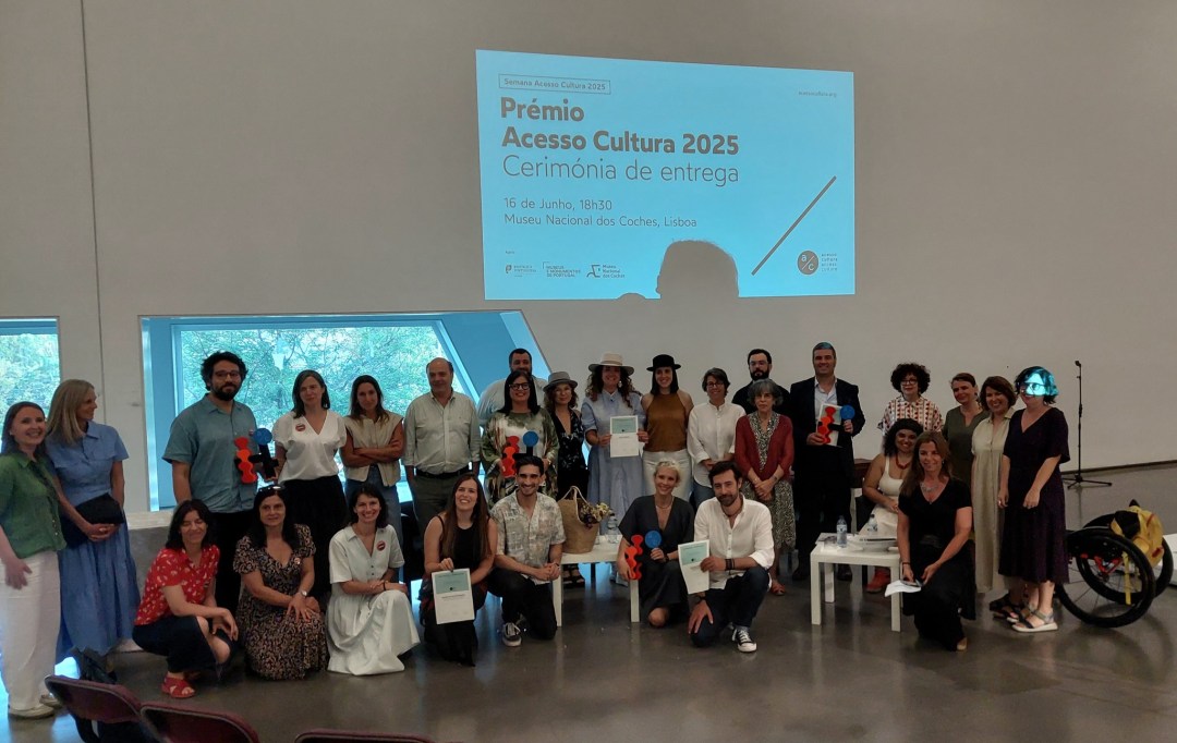 Fotografia de grupo dos premiados em frente ao slide que identifica o evento.